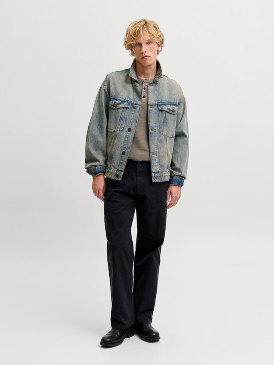 Model in olijfgroen Henley-shirt, oversized spijkerjas, zwarte broek en laarzen.