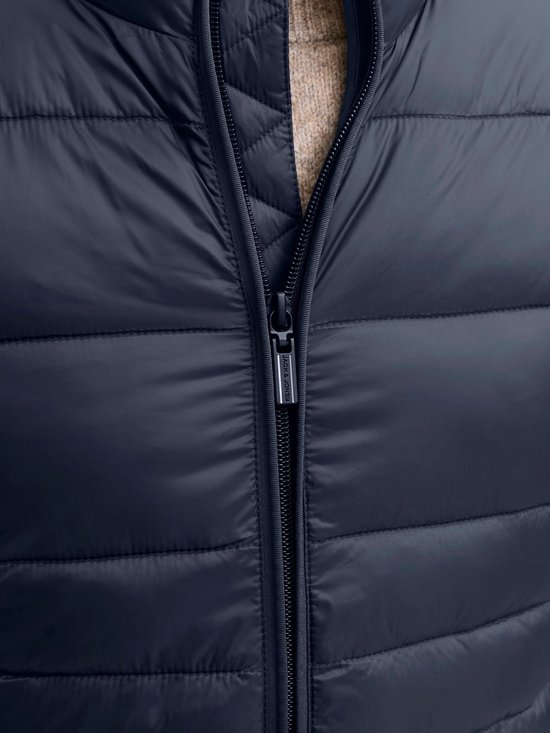 Close-up van de rits met het JACK & JONES logo op de ritssluiting van het donkerblauwe pufferjack.