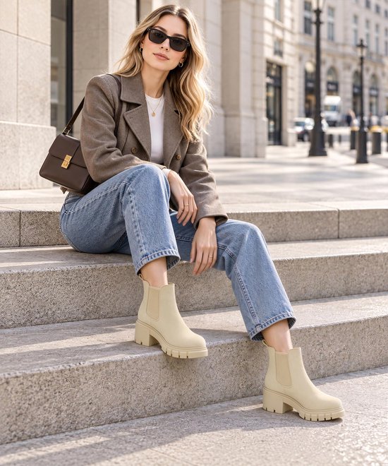 Model zittend op trappen in de stad, draagt beige Chelsea laarzen met blokhak onder een jeans.