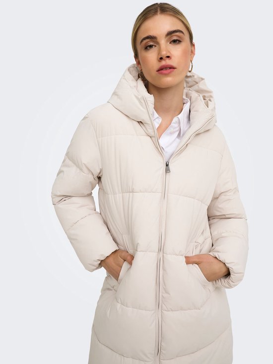 Model draagt een beige pufferjas met capuchon, rits en steekzakken over een wit overhemd.