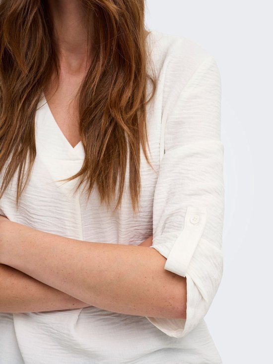 Detailopname van een witte blouse met opgerolde mouw, gedragen door een model.