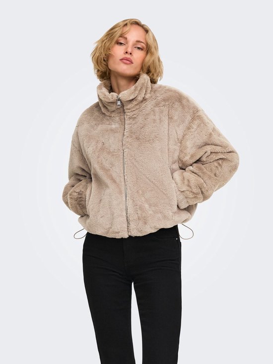 Model draagt een beige imitatiebont jack met opstaande kraag en ritssluiting, gecombineerd met zwarte broek.