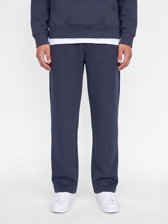 Model draagt een donkerblauwe joggingbroek met losse pasvorm, gecombineerd met een wit T-shirt.