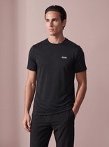 Vooraanzicht van een man in een zwart sportshirt met fijn gestreept patroon en SJS-logo, met hand in broekzak.