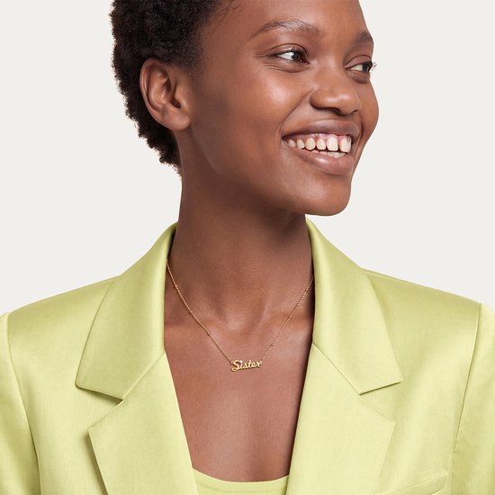 Lachend model met kort haar draagt een goudkleurige 'Sister'-ketting met zirkonia en een limoengroene blazer.