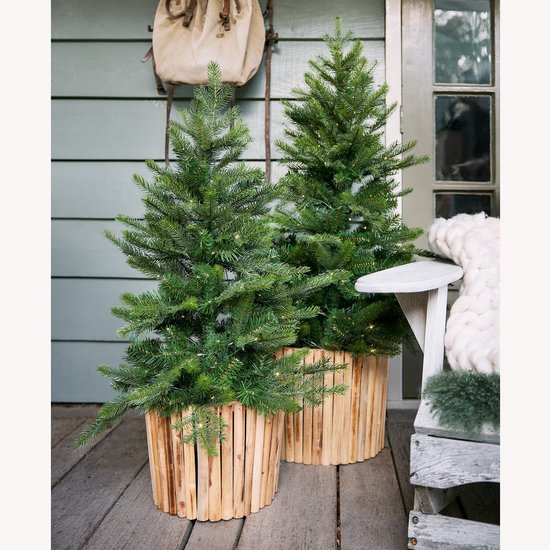 Twee kunstkerstbomen in houten manden op een veranda, verlicht met fijne LED-lichtjes.