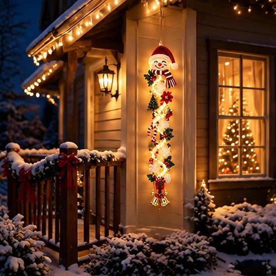 Verlichte sneeuwpop-deurhanger aan een buitenveranda in een besneeuwde kerstomgeving met warme verlichting.