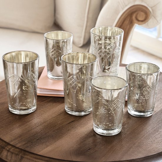 Zes glazen windlichten met een antieke zilverlook en fijn gegraveerde patronen, op een houten tafel geplaatst.