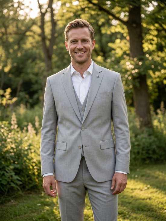 Man in driedelig grijs geweven pak met wit overhemd, staand in een groene tuin.
