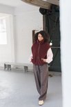 Model draagt een bordeauxrode wollen bodywarmer over een roze trui en donkere broek.