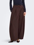 Model draagt een bruine wijde broek met plooien en een donkerblauw shirt met kanten mouwboorden.