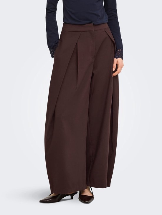 Model draagt een bruine wijde broek met plooien en een donkerblauw shirt met kanten mouwboorden.