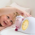 Lachend kind raakt roze schaap wekker aan met gele verlichting.