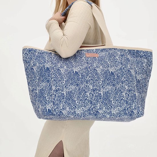 Grote XL strandtas met blauwe koraalprint en beige hengsels, gedragen door een model.