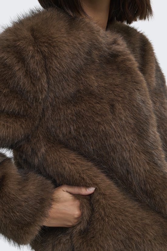 Detailopname van de textuur van het bruine imitatiebont, met de hand van het model in de zak.