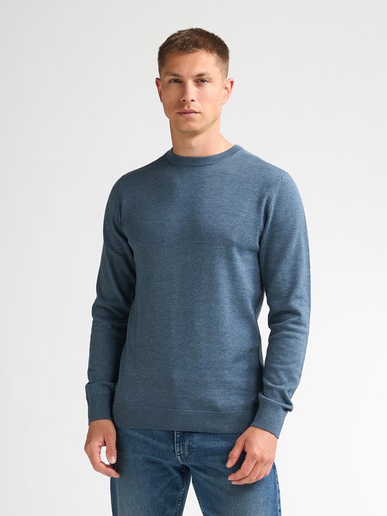 Een man draagt een blauwe, fijngebreide trui met ronde hals en een spijkerbroek.