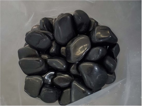 Een berg glanzende, zwarte kiezels in een plastic zak, met een witte achtergrond.