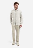 Model draagt een beige overhemd met verticale, brede witte en taupe strepen. Hij draagt er een beige pantalon bij.