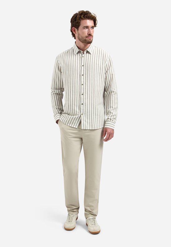 Model draagt een beige overhemd met verticale, brede witte en taupe strepen. Hij draagt er een beige pantalon bij.