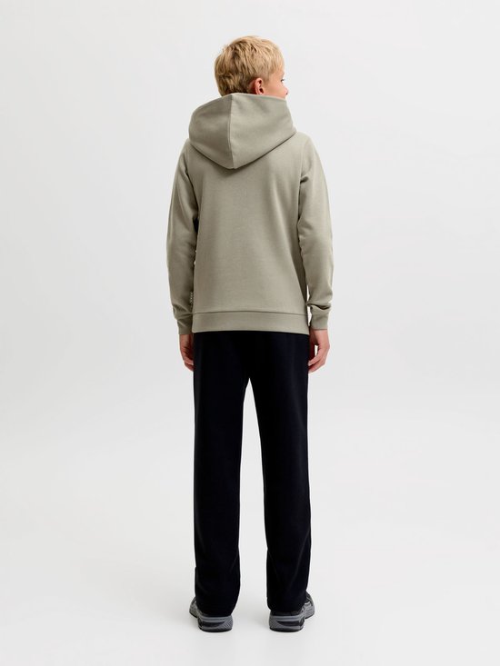 Jongen met blonde haren draagt een olijfgroene hoodie en zwarte joggingbroek. Zijaanzicht achter.