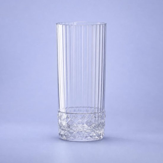 Transparant longdrinkglas met verticale ribbels en een gedetailleerd diamantpatroon aan de onderkant, op een paarse achtergrond.
