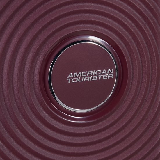 Detail van het "AMERICAN TOURISTER" logo op de bordeauxrode koffer met cirkelvormig patroon.