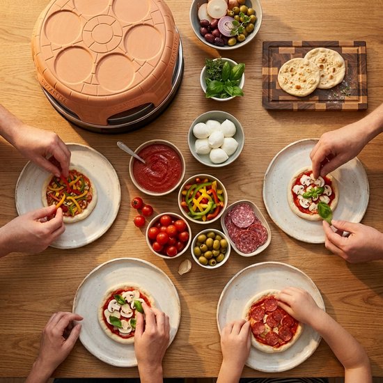 Bovenaanzicht van mensen die mini-pizza's beleggen rond een terracotta pizzaoven.