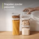 Une main ferme un bocal Safecourt rempli d'amandes sur une pile d'autres bocaux remplis de spaghettis, muesli et riz.