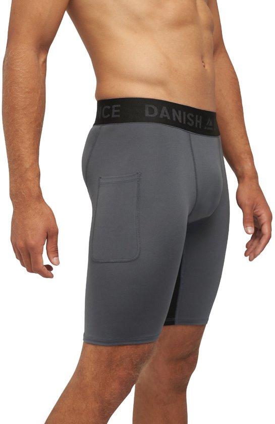 Man draagt een donkergrijze lange sportbroek met elastische tailleband met logo. De broek heeft een zak op de heup.