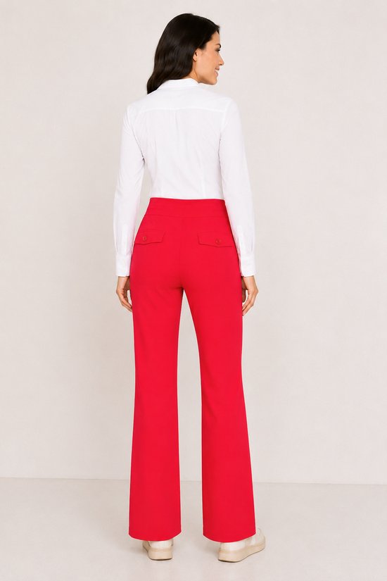 Model met lange mouwen in witte blouse en rode flared broek met opgestikte achterzakken.