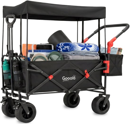Chariot de plage noir Gooala avec auvent, rempli d'un tapis, coussins, assiettes, couverture et bouteilles d'eau.