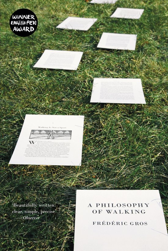 Een boek met de titel 'A PHILOSOPHY OF WALKING' van FRÉDÉRIC GROS ligt op gras, met uitklapbare pagina's waarop tekst staat.