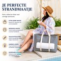Vrouw met gestreepte kaftan en strooien hoed bij zwembad, naast blauw-wit gestreepte strandtas met handdoek.