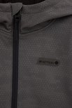Close-up van de voorkant van een donkergrijze softshell jas met capuchon. De jas heeft een subtiel geometrisch patroon en een logo met tekst 'DEFINED BY MOTION'.