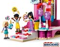 Drie LEGO Friends poppetjes staan op de trap van het reuzenrad, met een blauwe narwal en een donut.