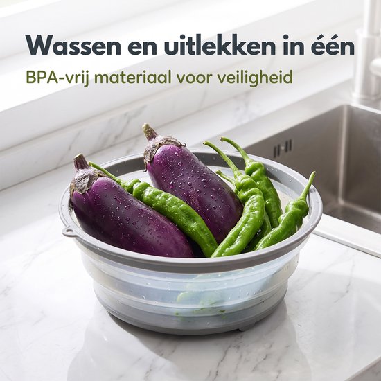Grijze, opvouwbare kom met aubergines, pepers en komkommers, met kraan en gootsteen op de achtergrond.