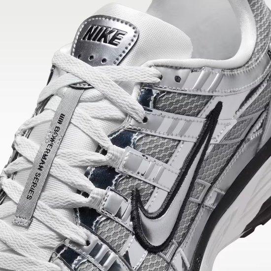 Close-up van de grijze Nike P-6000 sneaker. Zwarte Nike swoosh en 'NIKE' logo op de tong. Witte veters.