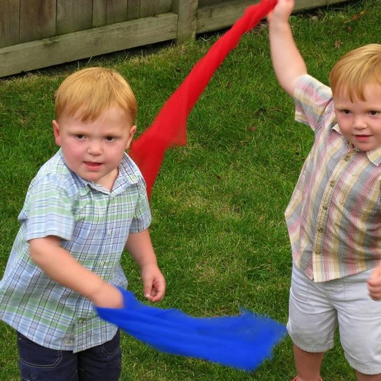 Twee jonge jongens buiten met een rode en een blauwe chiffon sjaal. De jongen links speelt met een blauwe sjaal, de jongen rechts houdt een rode sjaal omhoog.
