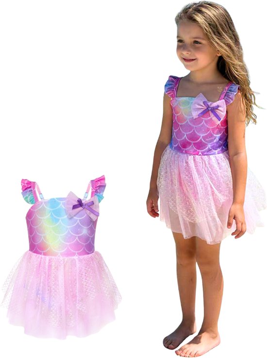 Meisje op het strand naast een roze badpakjurk met regenboog schubbenprint en tule rok.
