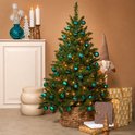 Groene kunstkerstboom versierd met teal kerstballen en lichtjes, naast een open haard.