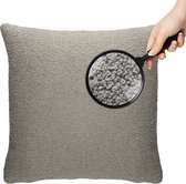 Hand houdt vergrootglas vast boven grijs teddy kussen. De textuur van het kussen is zichtbaar.