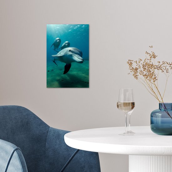 Trois dauphins nagent sous l'eau dans une eau bleue avec des rayons de soleil, accrochés à un mur au-dessus d'une table.