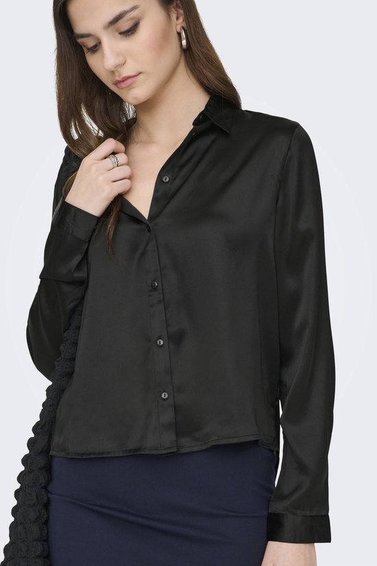 Model draagt zwarte satijnen blouse met knoopjes en donkerblauwe rok.