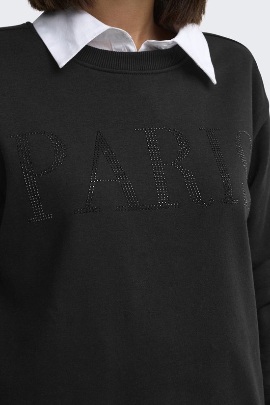 Close-up van zwarte sweater met "PARIS" opdruk van parels, met wit overhemd.