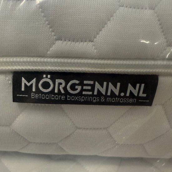 Close-up van Mörgenn.nl label op een witte, gewatteerde textiel met hexagonale patronen.