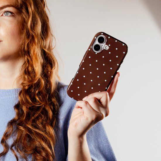 Vrouw met krullend rood haar houdt een bruin telefoonhoesje met polkadots vast.