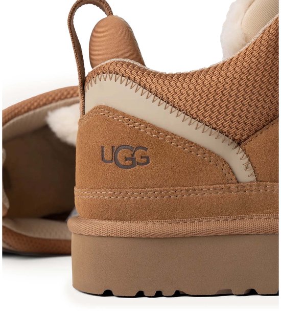 Zijaanzicht van een bruine UGG sneaker met suède en mesh materiaal, een dikke zool en UGG logo op de hiel.