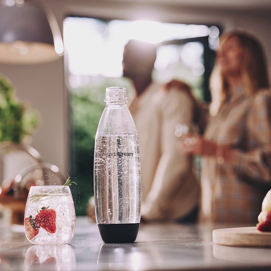Sodastream fles van helder plastic met zwarte dop en onderkant, naast een glas met aardbeien.