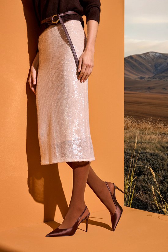 Een vrouw draagt een beige pailletten rok, bruine panty en bruine pumps.