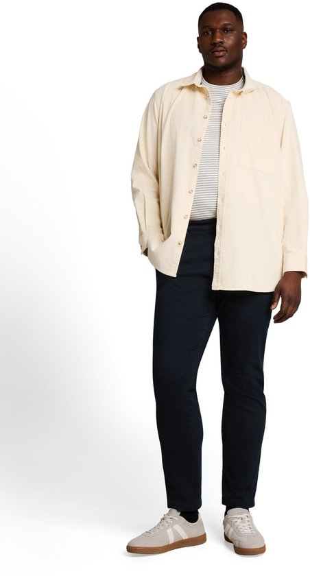 Model draagt een marineblauwe chino met een beige overhemd, gestreept shirt en beige sneakers.